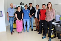 Gruppe von sieben Menschen stehen nebeneinander in einem Labor vor einer Maschine im Hintergrund